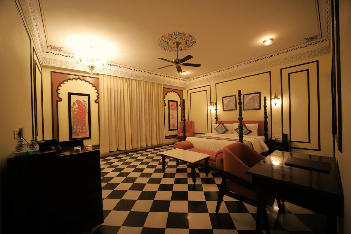 Habitación de hotel con piso a cuadros, cama con cabecera roja, escritorio y ventilador de techo.