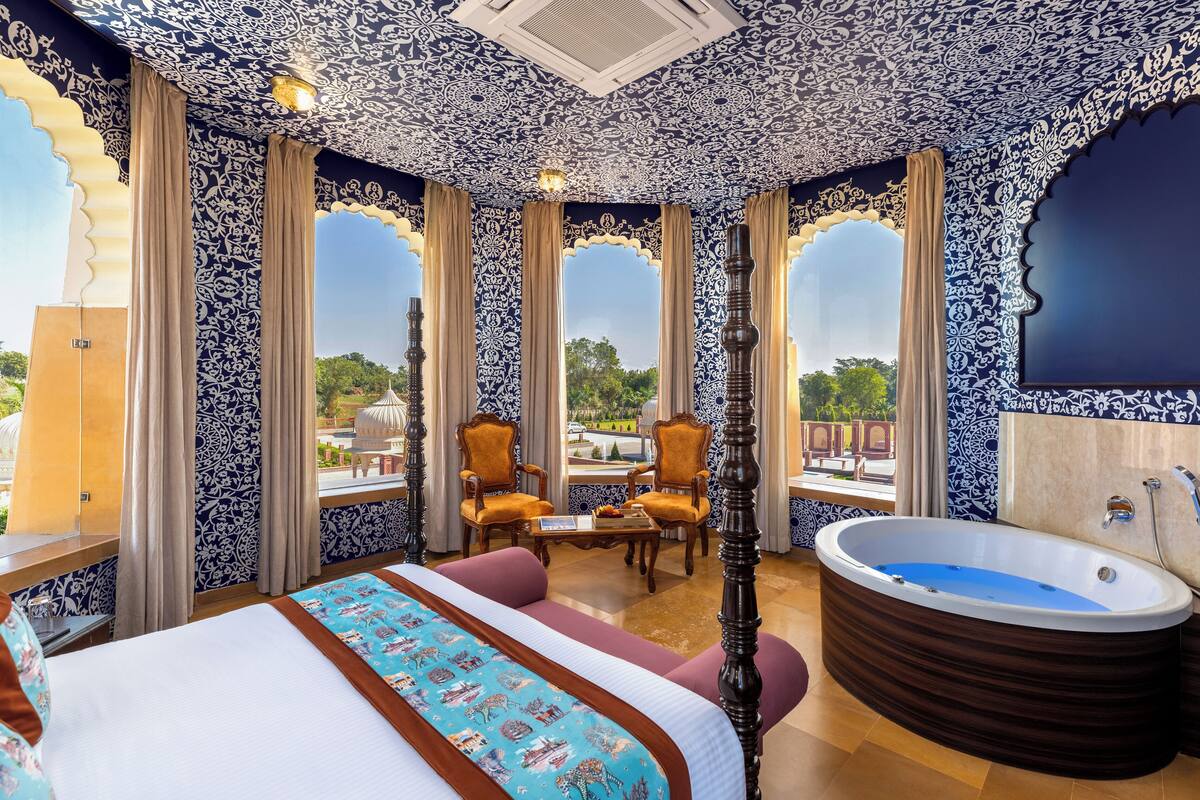 Un dormitorio lujoso con una cama grande, una zona de estar con sillones, una bañera y ventanas amplias que ofrecen vistas al exterior.