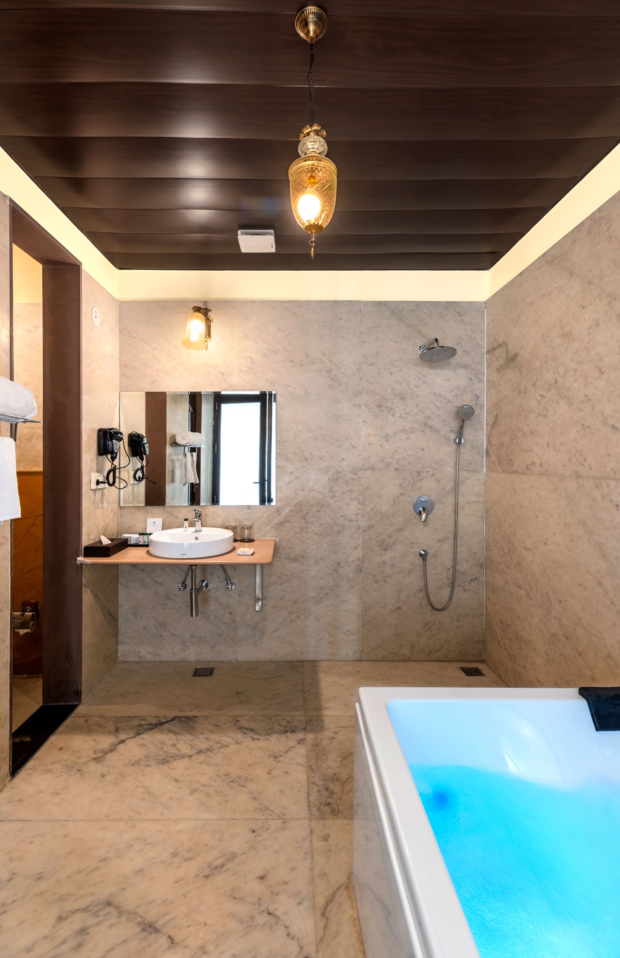 Une salle de bain moderne avec un sol en marbre, une grande baignoire, un lavabo avec un miroir, une douche et un luminaire au plafond.