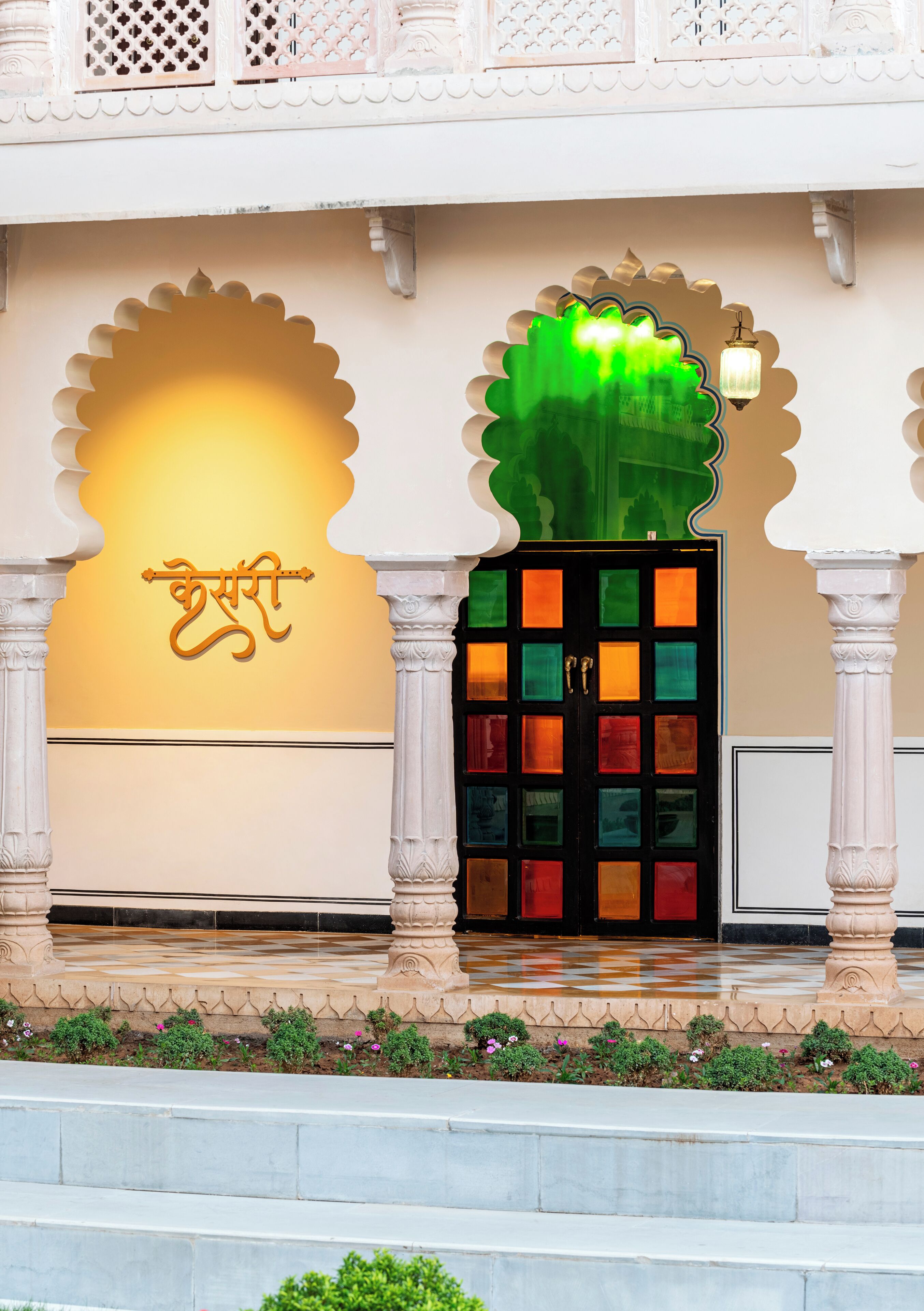 Un edificio tradicional con un amplio arco de entrada, una pared decorativa con un emblema dorado y una puerta colorida con un panel de vidrio verde.
