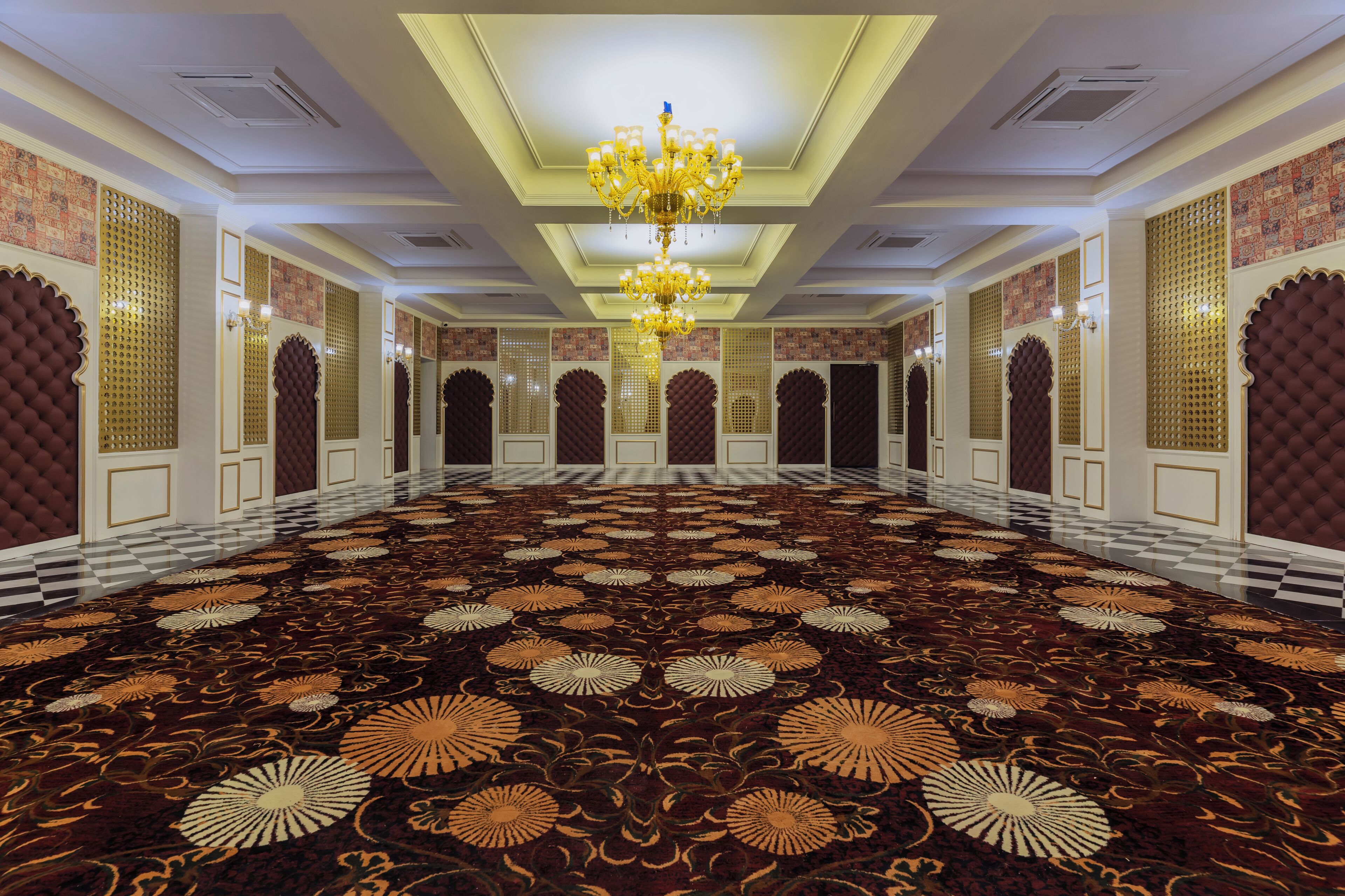 Un vaste hall d’hôtel, agrémenté d’un grand lustre, de panneaux muraux richement décorés et d’un tapis à motifs.