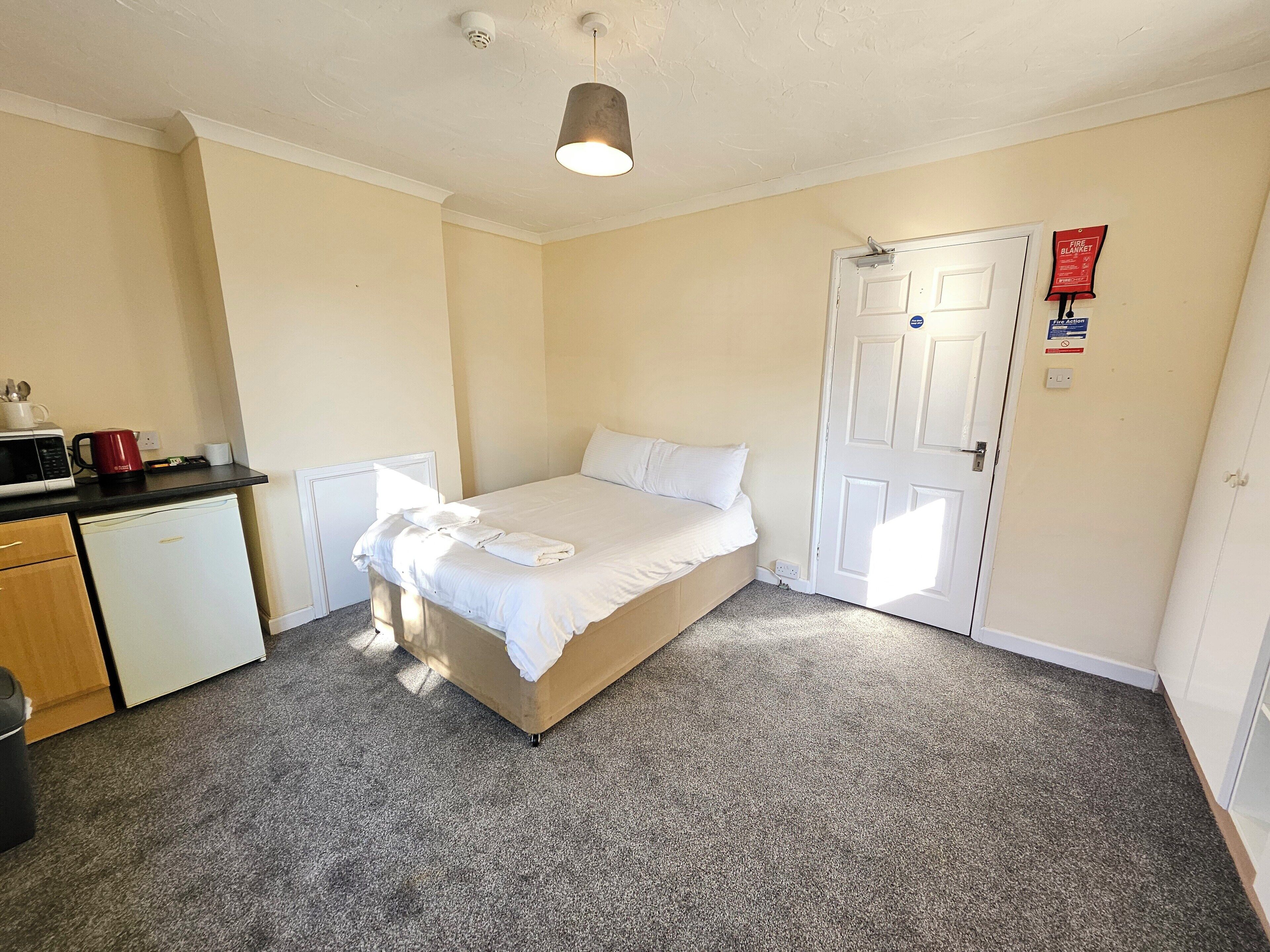 A small, clean room with a bed, a desk, and a microwave.