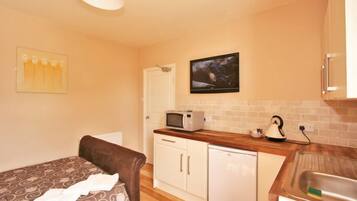 A compact room with a bed, a kitchenette with a microwave, a kettle, and a small refrigerator.