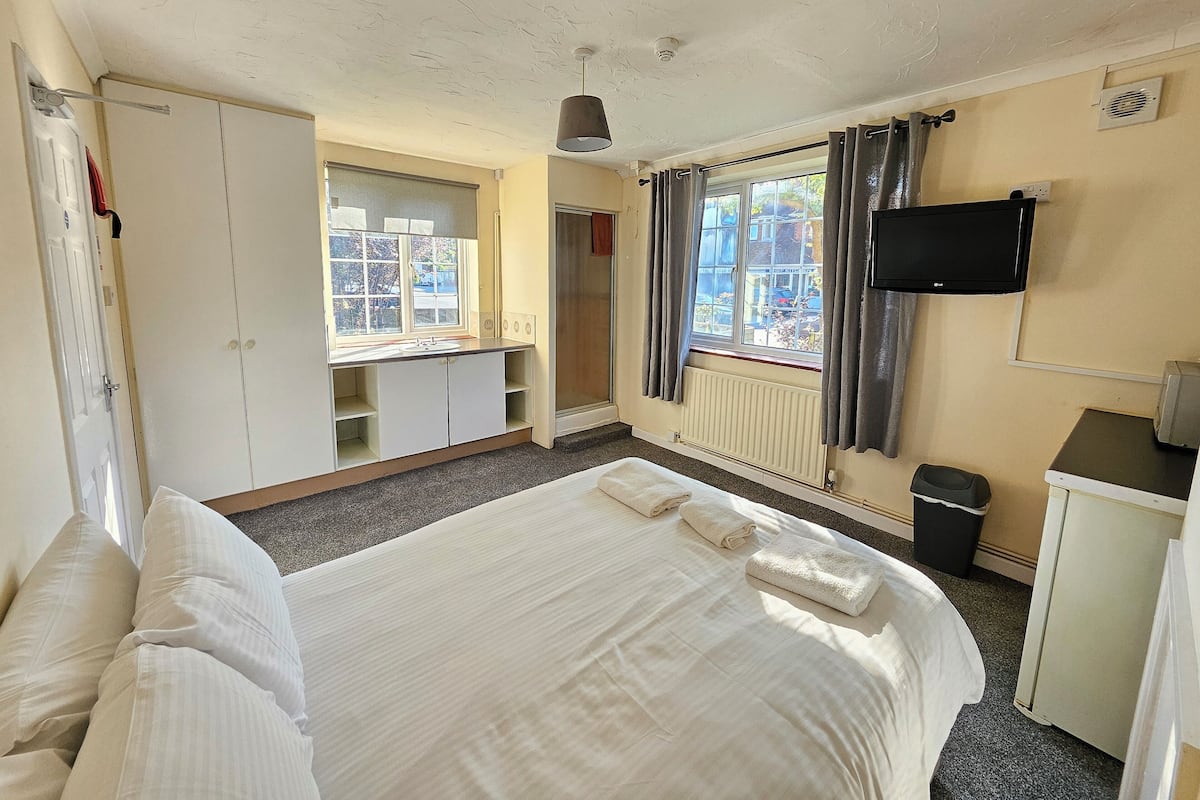 A hotel room with a bed, a desk, a window with curtains, a television, and a radiator.
