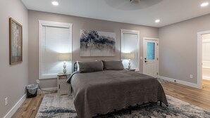 Un dormitorio con una cama, dos mesitas de noche, una lámpara de pared, un cuadro y una puerta con pomo azul.