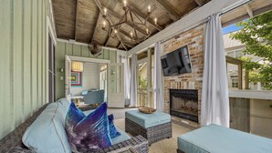 A cozy outdoor seating area with wicker furniture and cushions, a brick fireplace, and a ceiling fan.