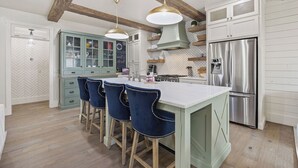 A kitchen with a central island, bar stools, a stainless steel refrigerator, and wooden beams on the ceiling.