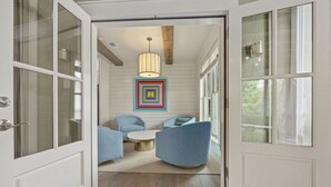 A hallway leading to a dining area with a modern chandelier, blue chairs, and a colorful geometric wall art piece.