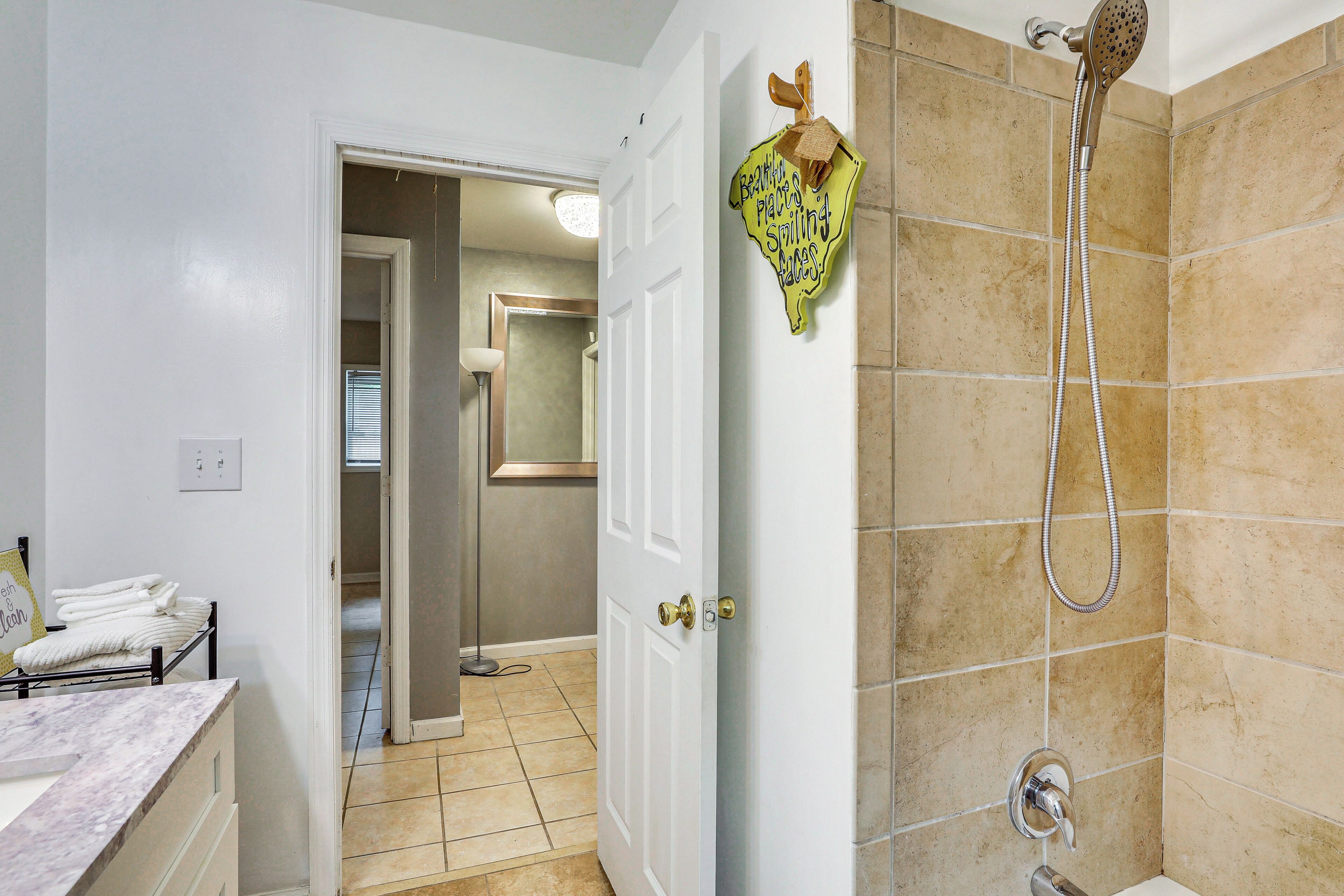 A bathroom with a shower, a towel rack with towels, and a door leading to another room.