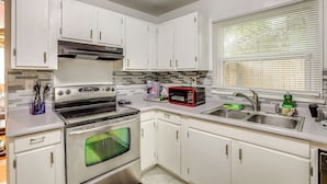 Una cocina con armarios blancos, horno de acero inoxidable, microondas y pileta.