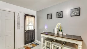Un pasillo con una puerta blanca, otra oscura, un banco blanco con asientos acolchados y una lámpara fijada a la pared.