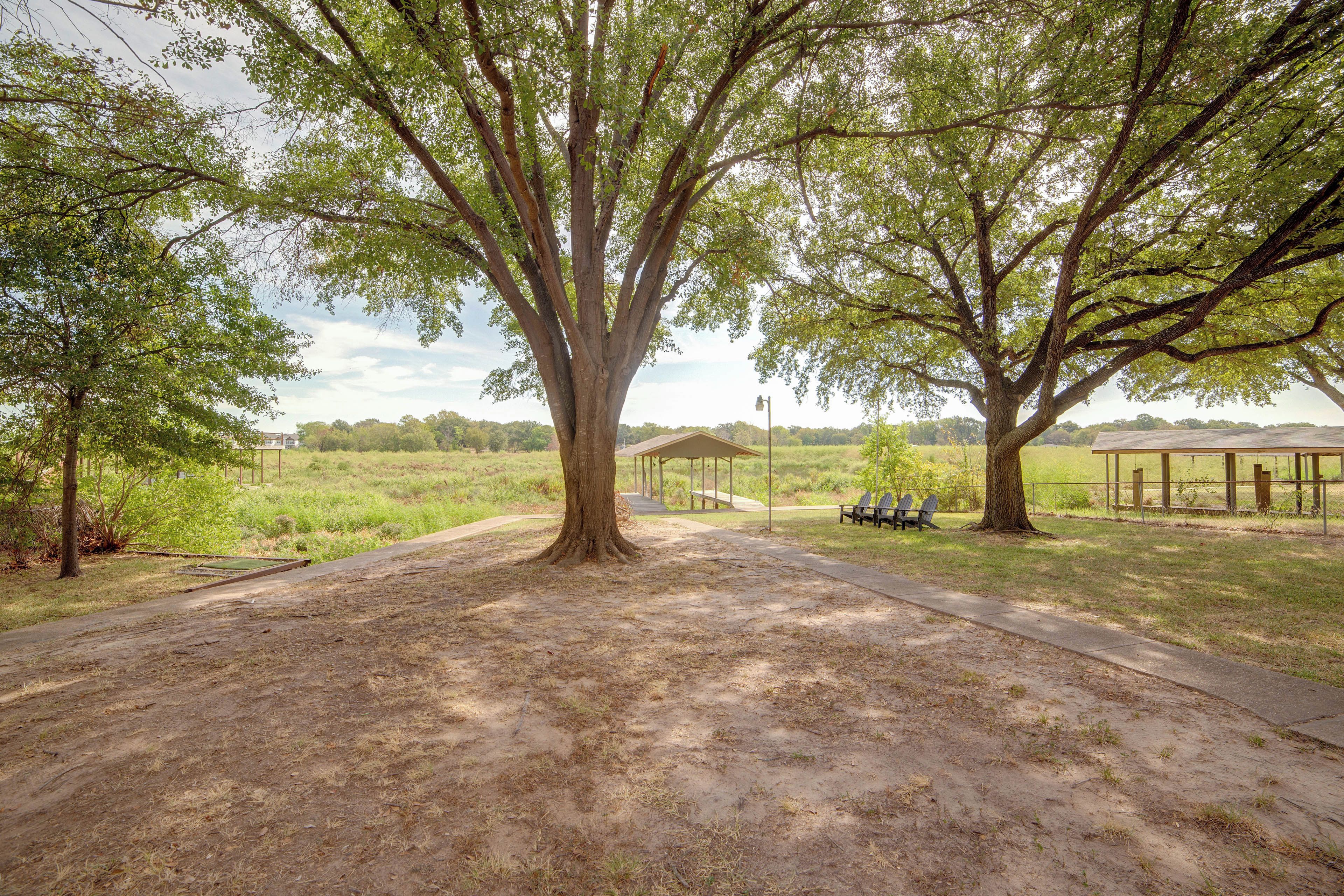 A park with a large tree, a covered picnic area, and a dirt path.