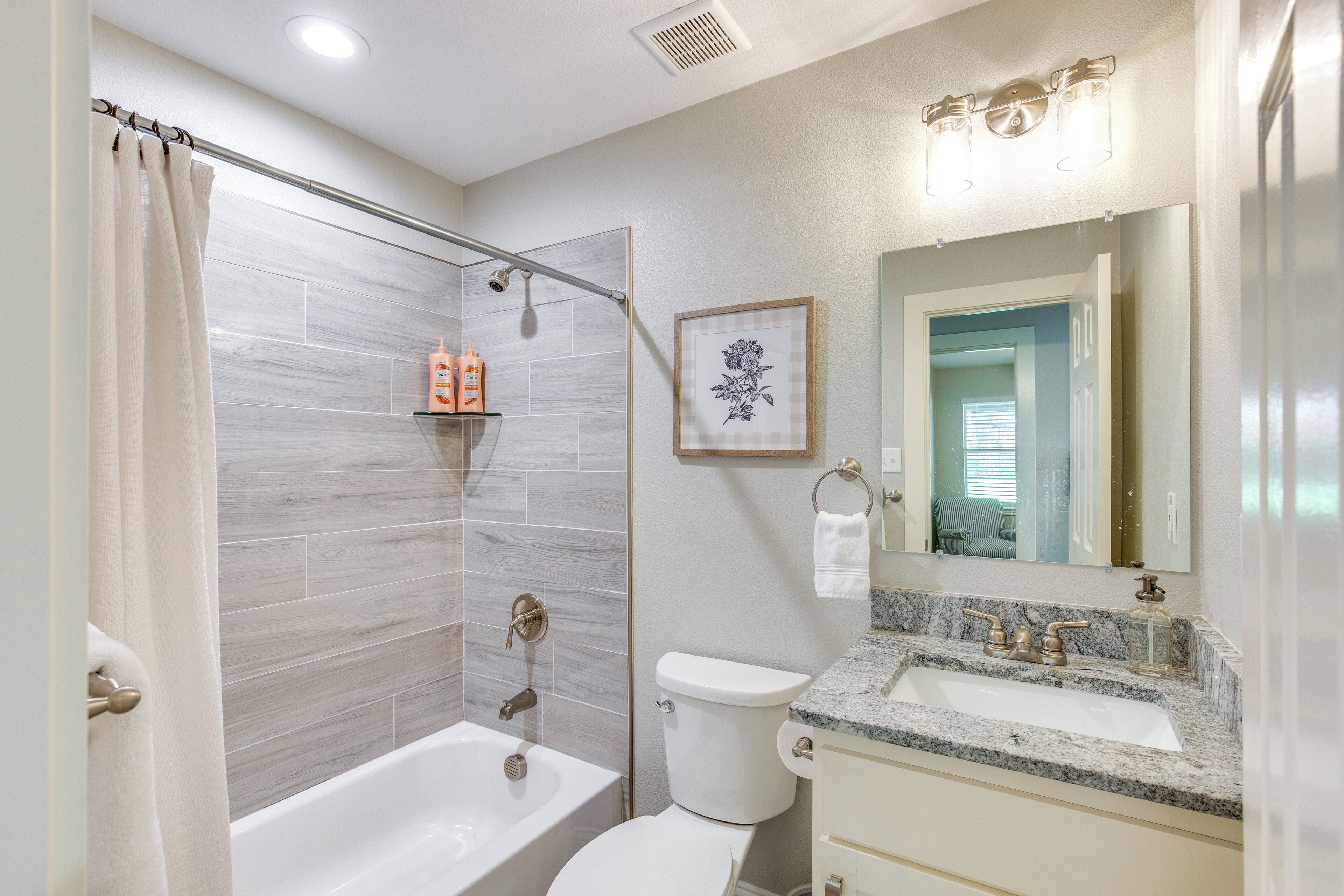 A bathroom with a bathtub, toilet, and sink. There is a shower curtain, a framed picture on the wall, and a mirror above the sink.