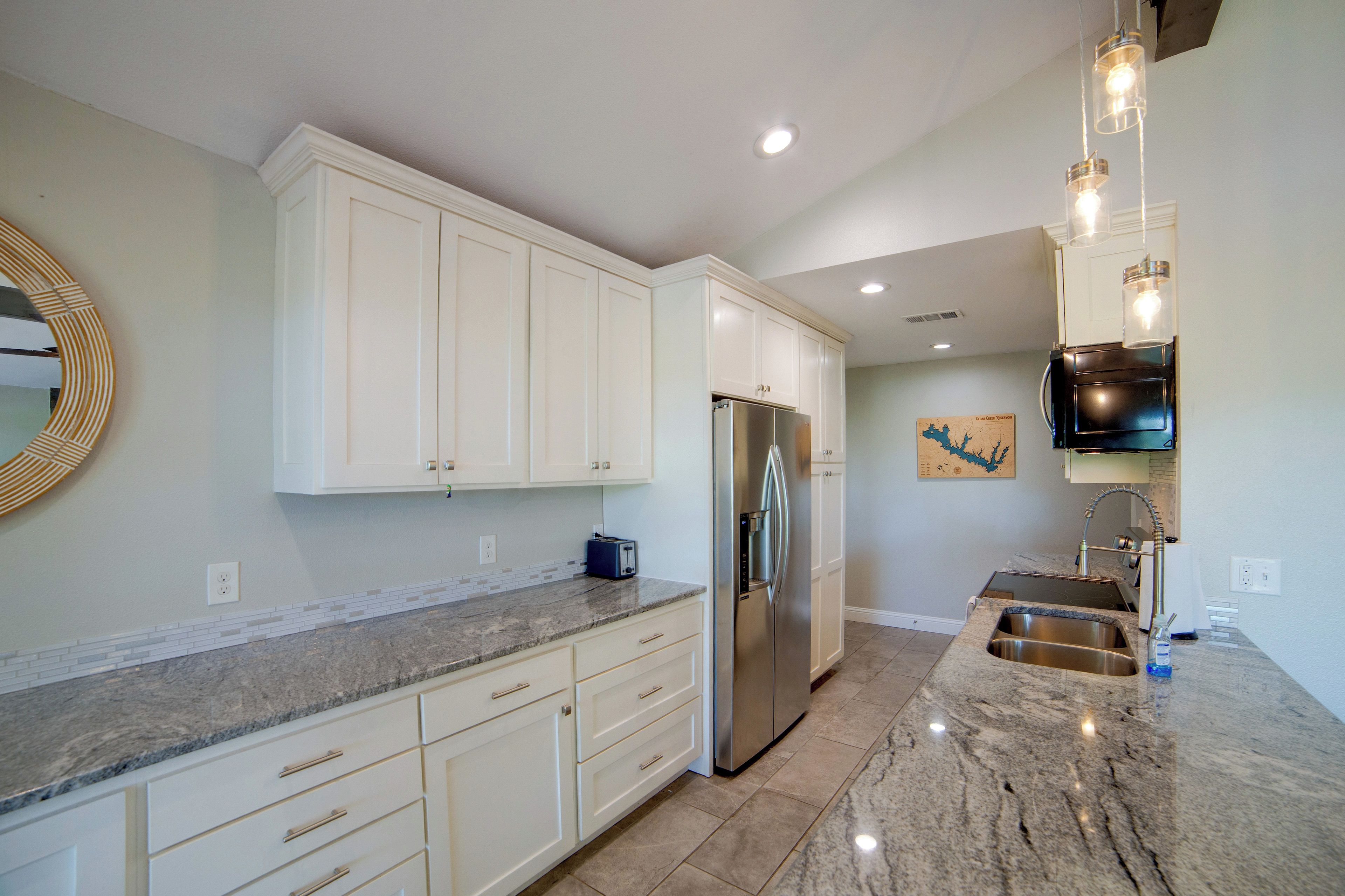 A modern kitchen with white cabinets, a stainless steel refrigerator, a granite countertop, and a built-in oven.