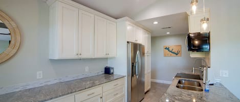 A modern kitchen with white cabinets, a stainless steel refrigerator, a granite countertop, and a built-in oven.