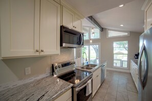 A modern kitchen with white cabinetry, stainless steel appliances, and a large window providing natural light. - Yard, Deck & Fire Pit: Cedar Creek Reservoir Gem (Mabank)