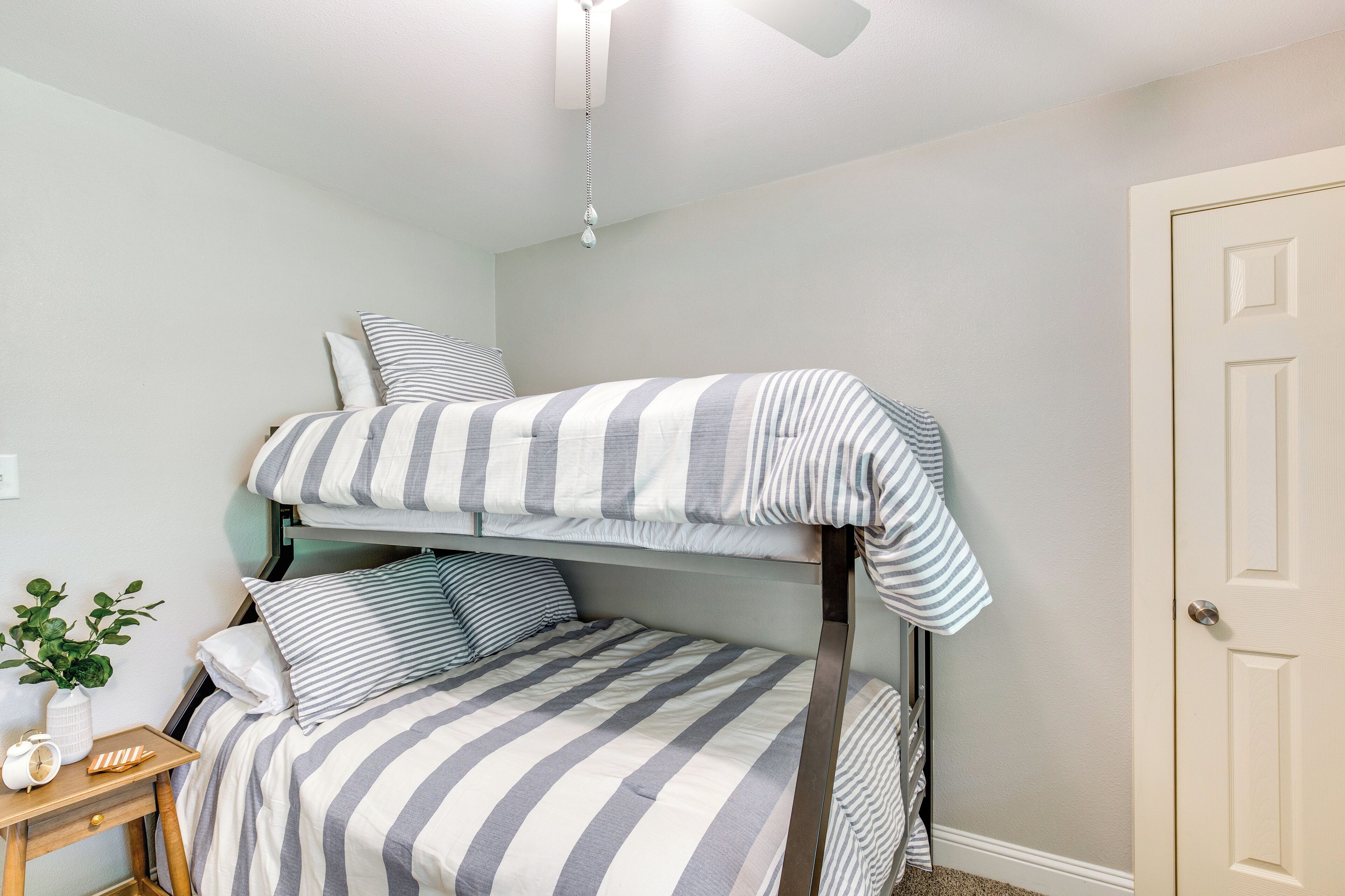 A bunk bed with striped bedding in a room with a small bedside table, a plant, and a door.