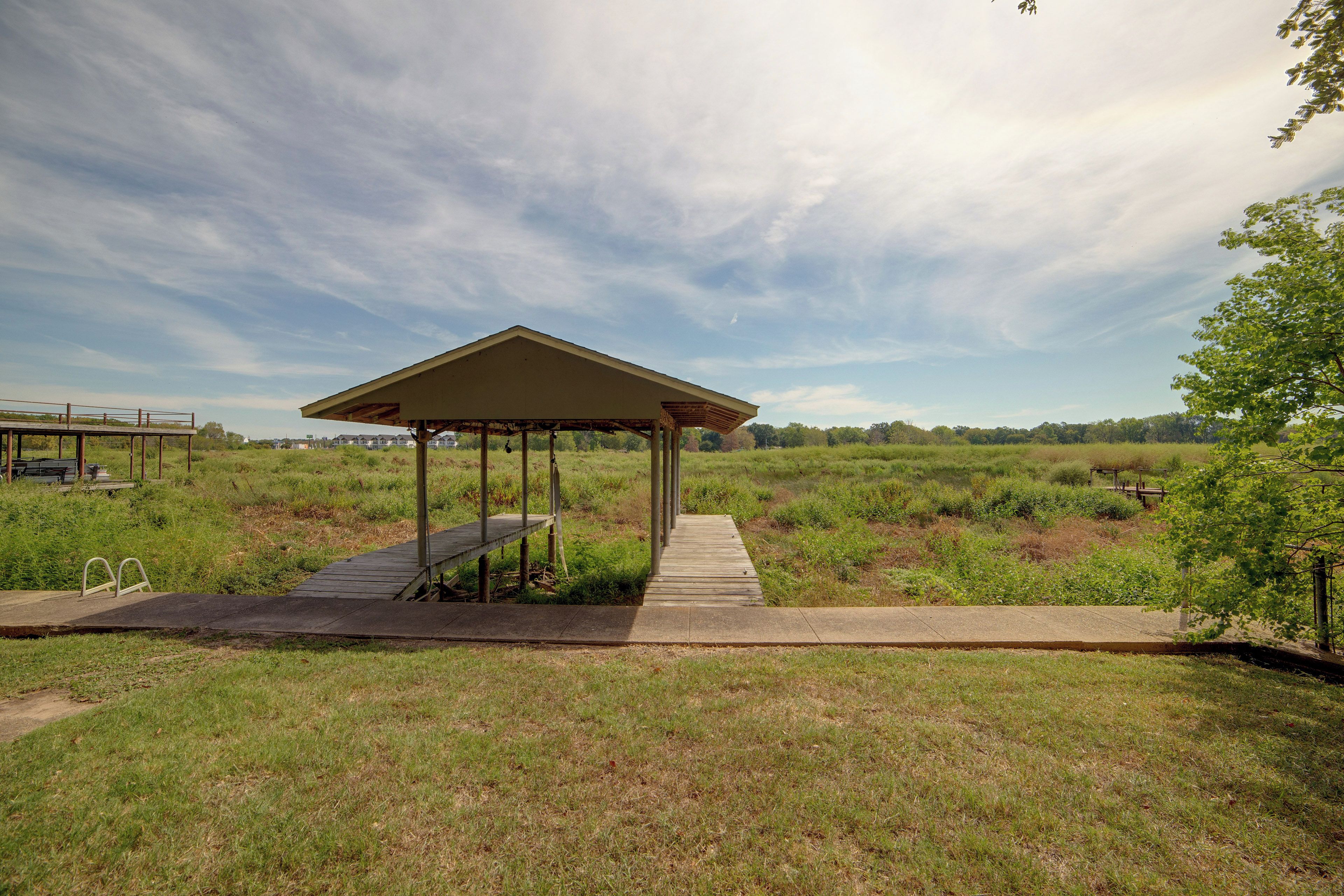 A gazebo with a concrete platform leading to it, surrounded by grassy fields and trees.