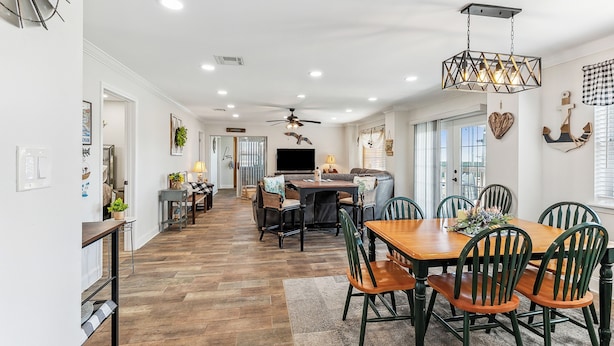 A spacious dining area with a wooden table and chairs, a ceiling fan, and a modern chandelier.