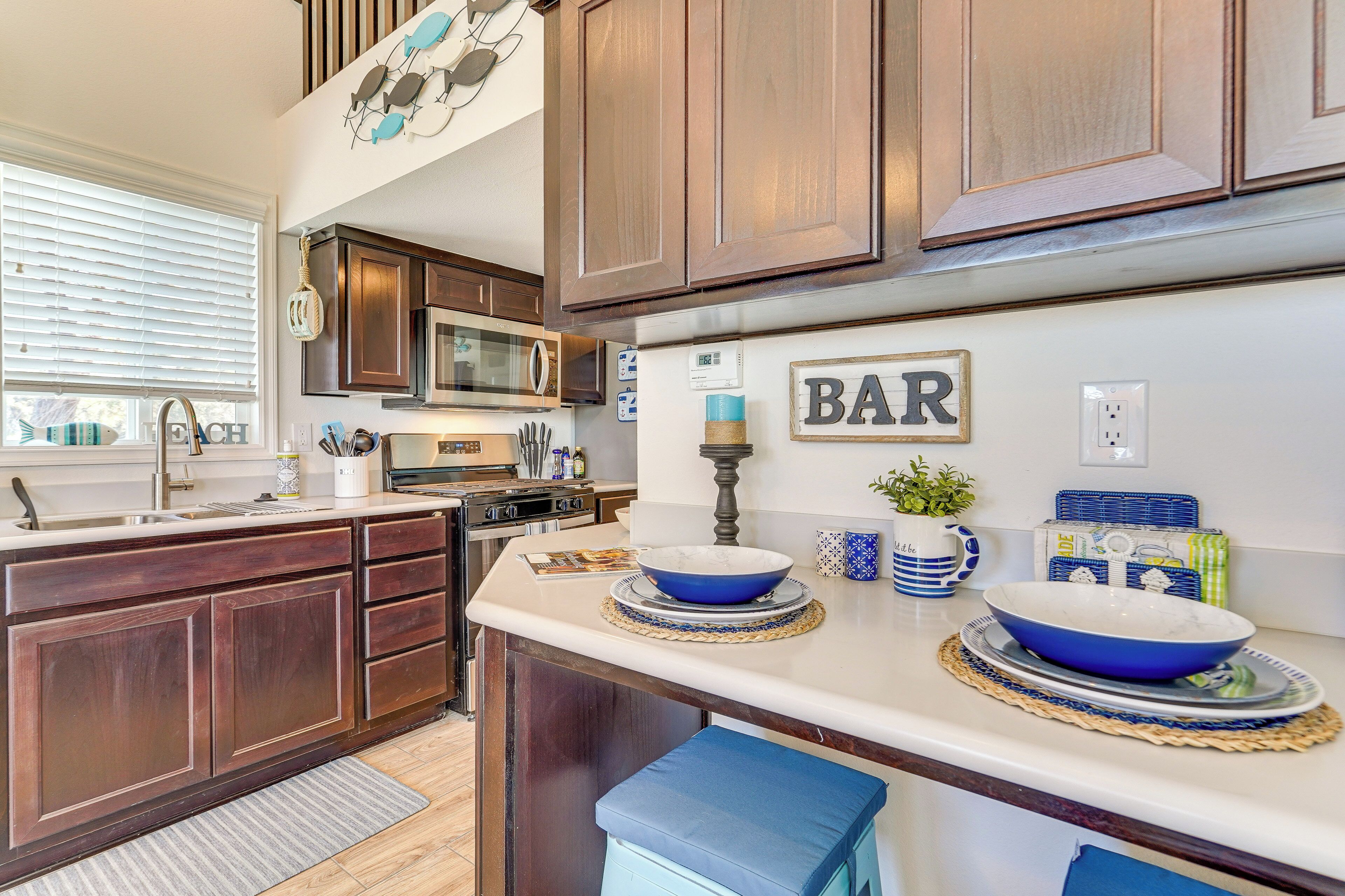 A kitchen with wooden cabinets, a microwave, a sink, and a countertop with blue bowls and a 'BAR' sign.