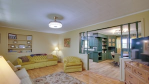 Ein geräumiges Wohnzimmer mit einem gelben Sofa, einem gemusterten Teppich und Holzböden.