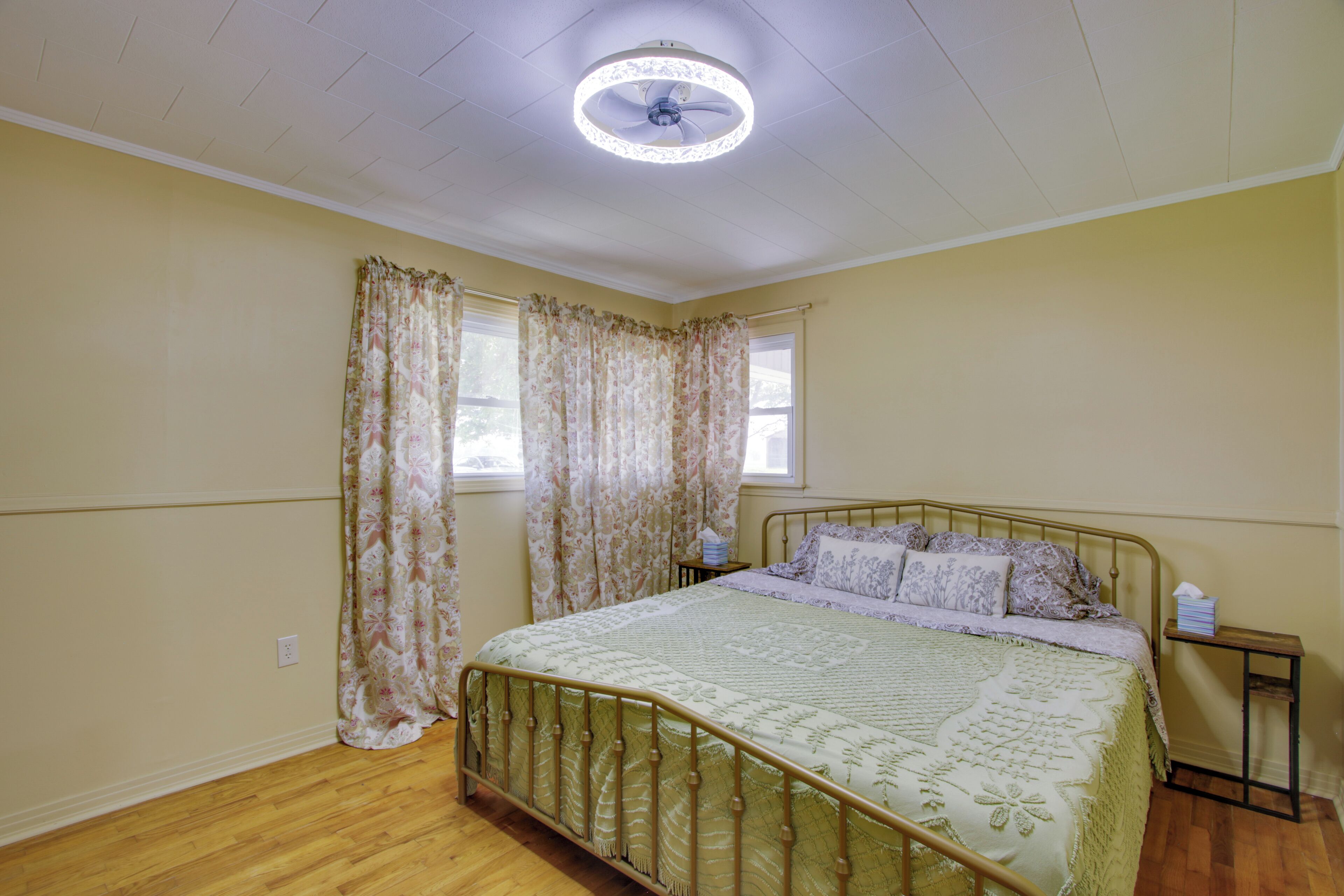A bedroom with a bed, curtains, a ceiling fan, and a nightstand.
