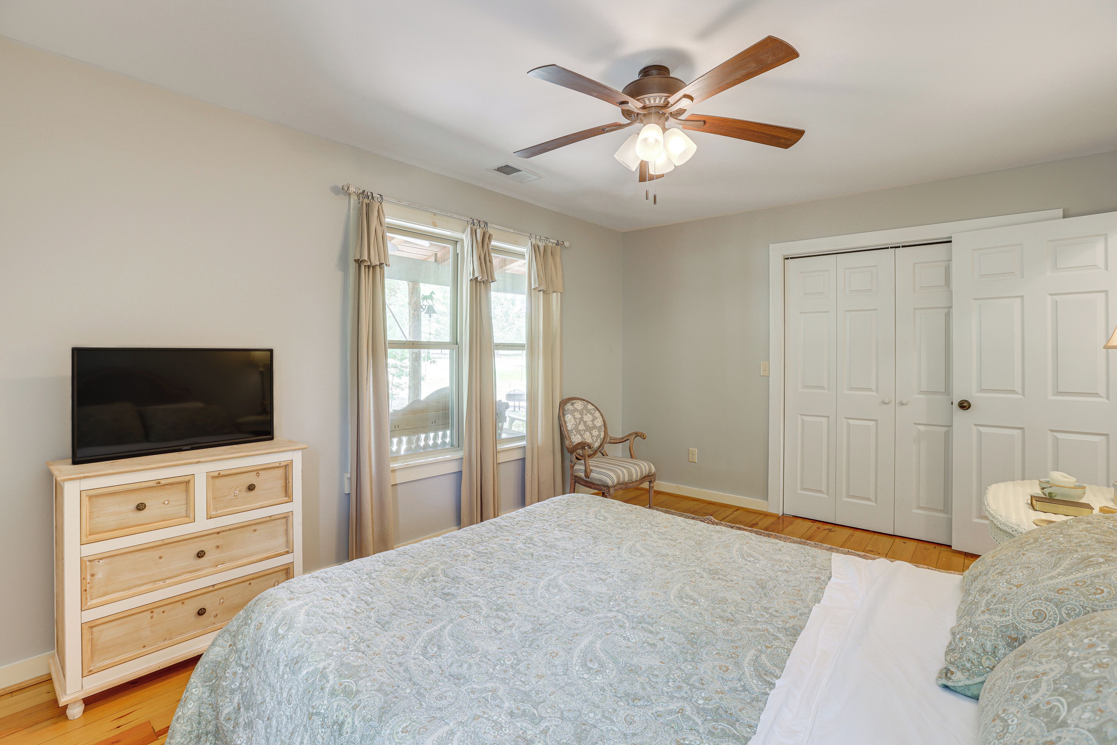 A bedroom with a bed, a dresser, a television, a chair, and a ceiling fan.