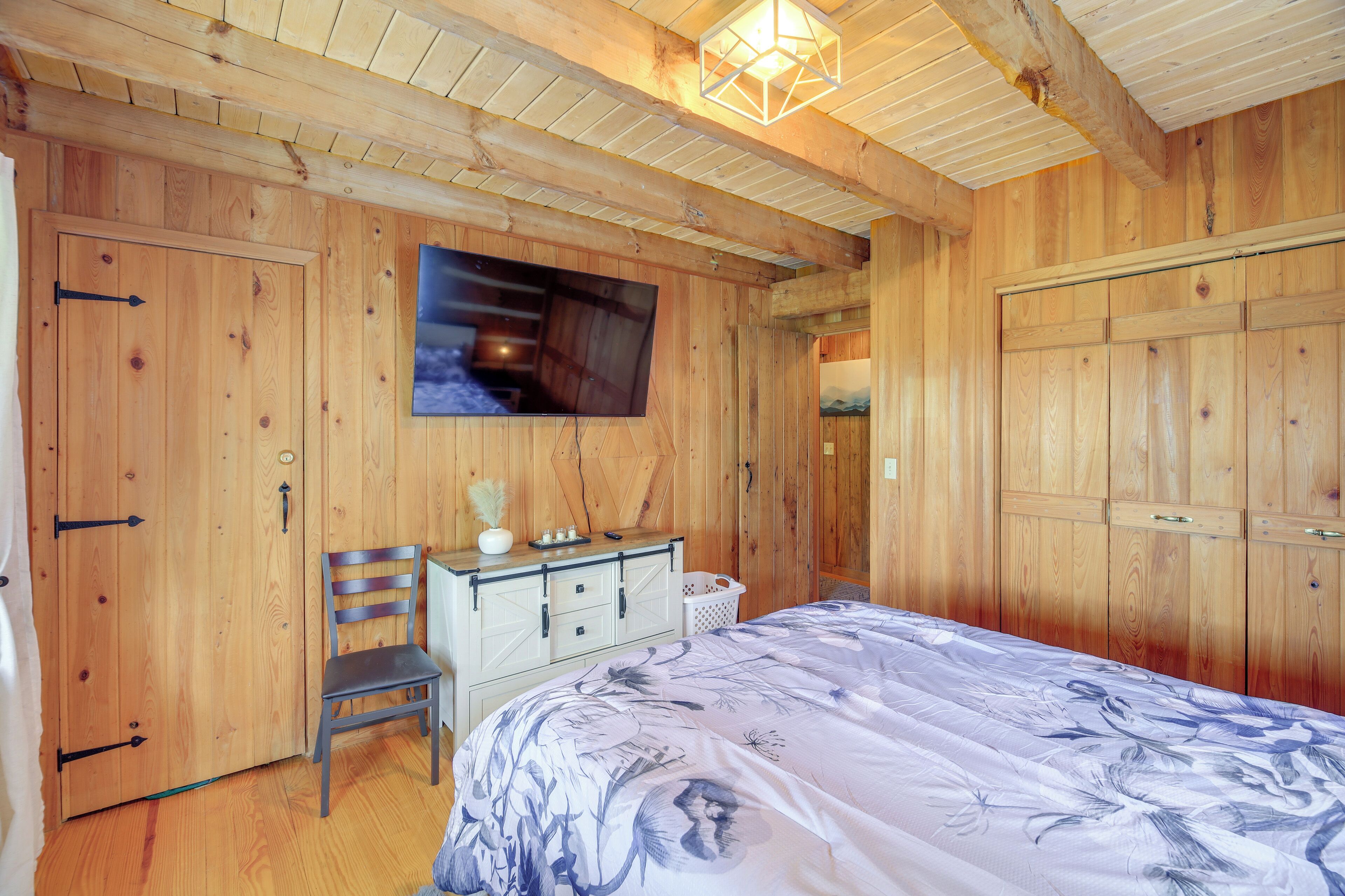 Een houten kamer met een bed, een dressoir, een stoel en een televisie aan de muur.