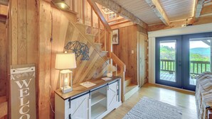 Een houten interieur met een trap, een welkomstbord, een lamp en uitzicht door een glazen deur.