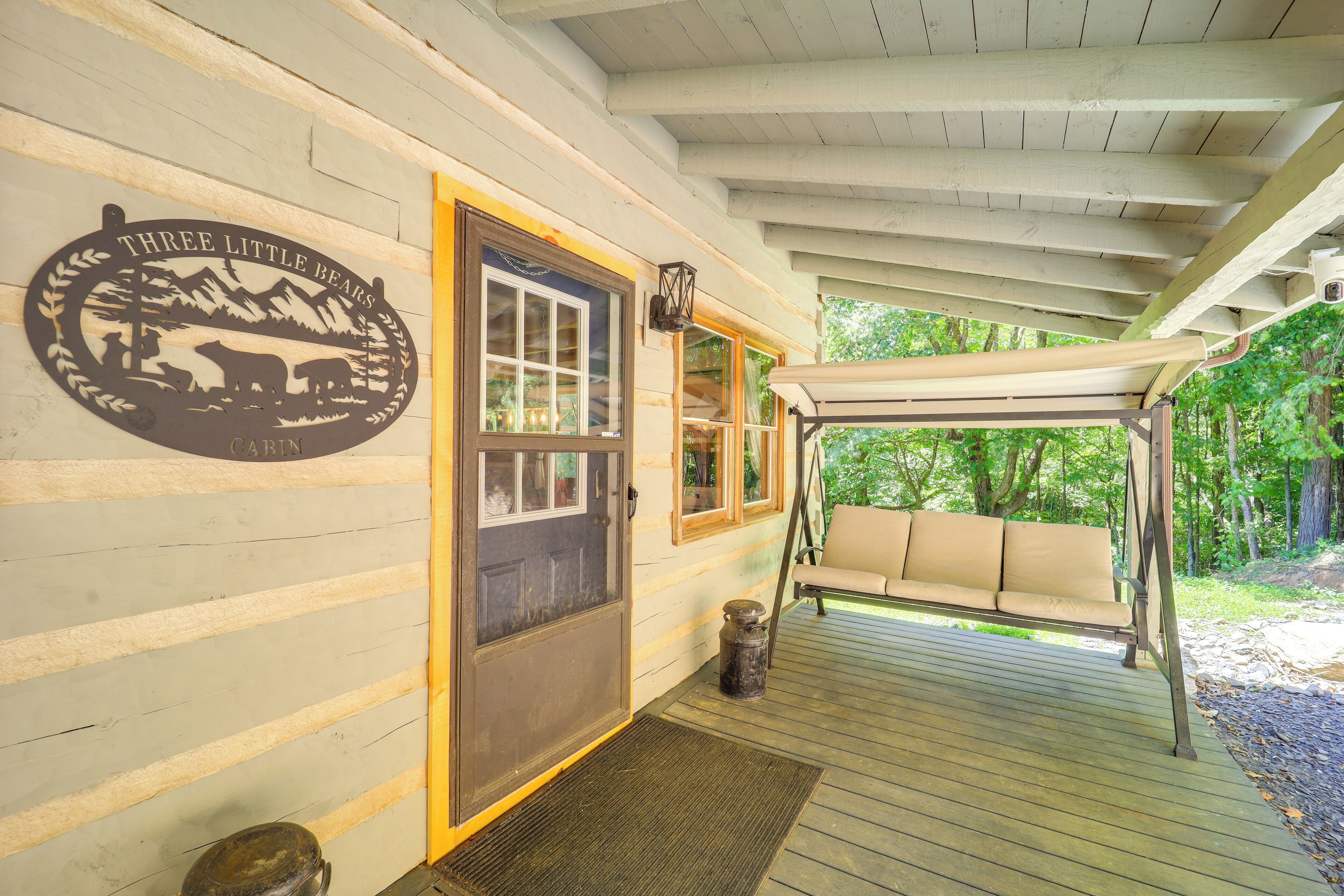 A cabin entrance with a swing chair, a door with a bear logo, and a covered porch.