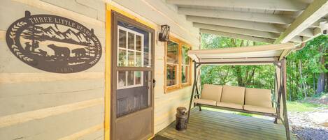 A cabin entrance with a swing chair, a door with a bear logo, and a covered porch.