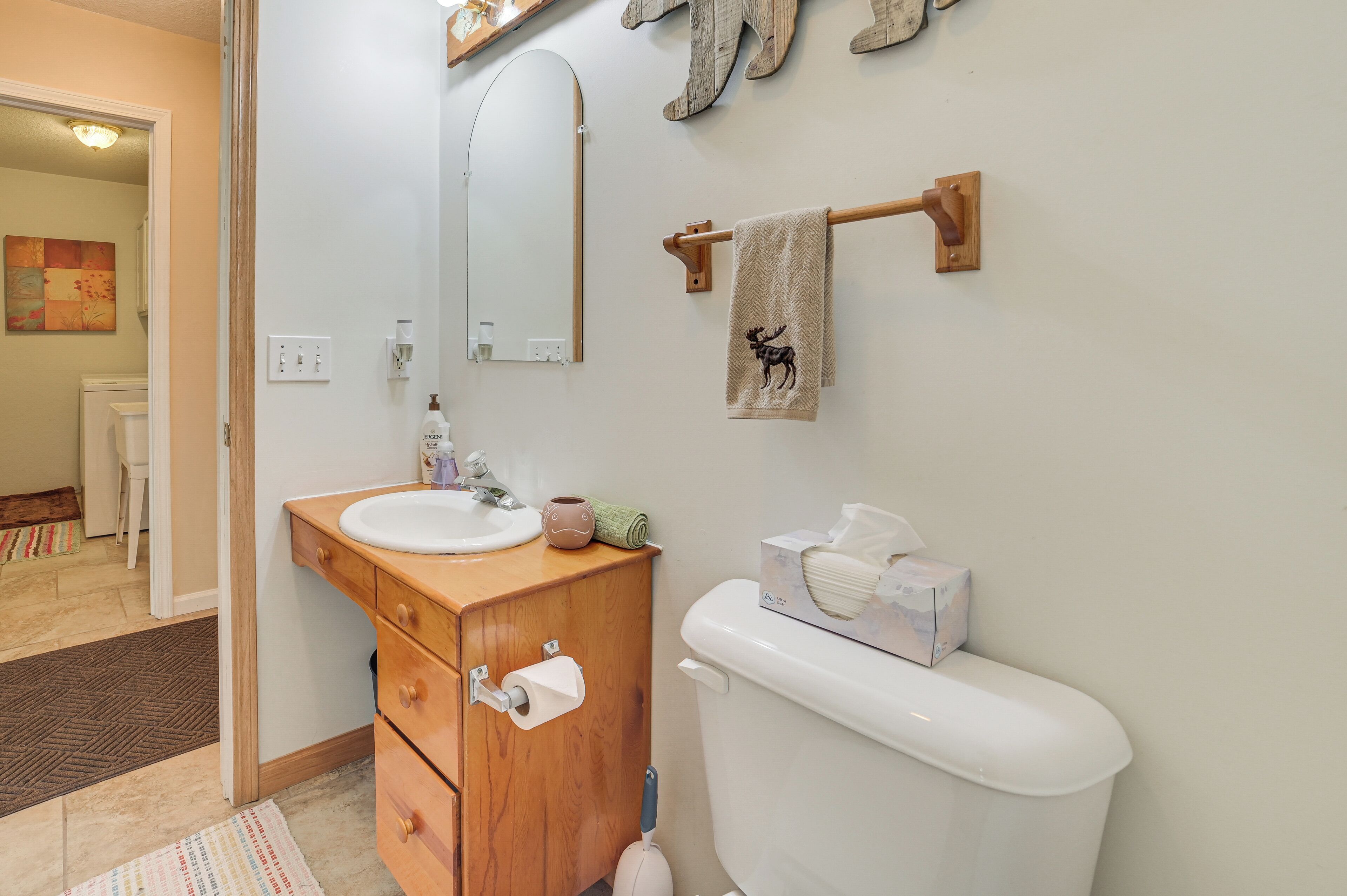 A bathroom with a wooden vanity, white sink, and toilet. There is a towel with a moose design hanging on the wall.