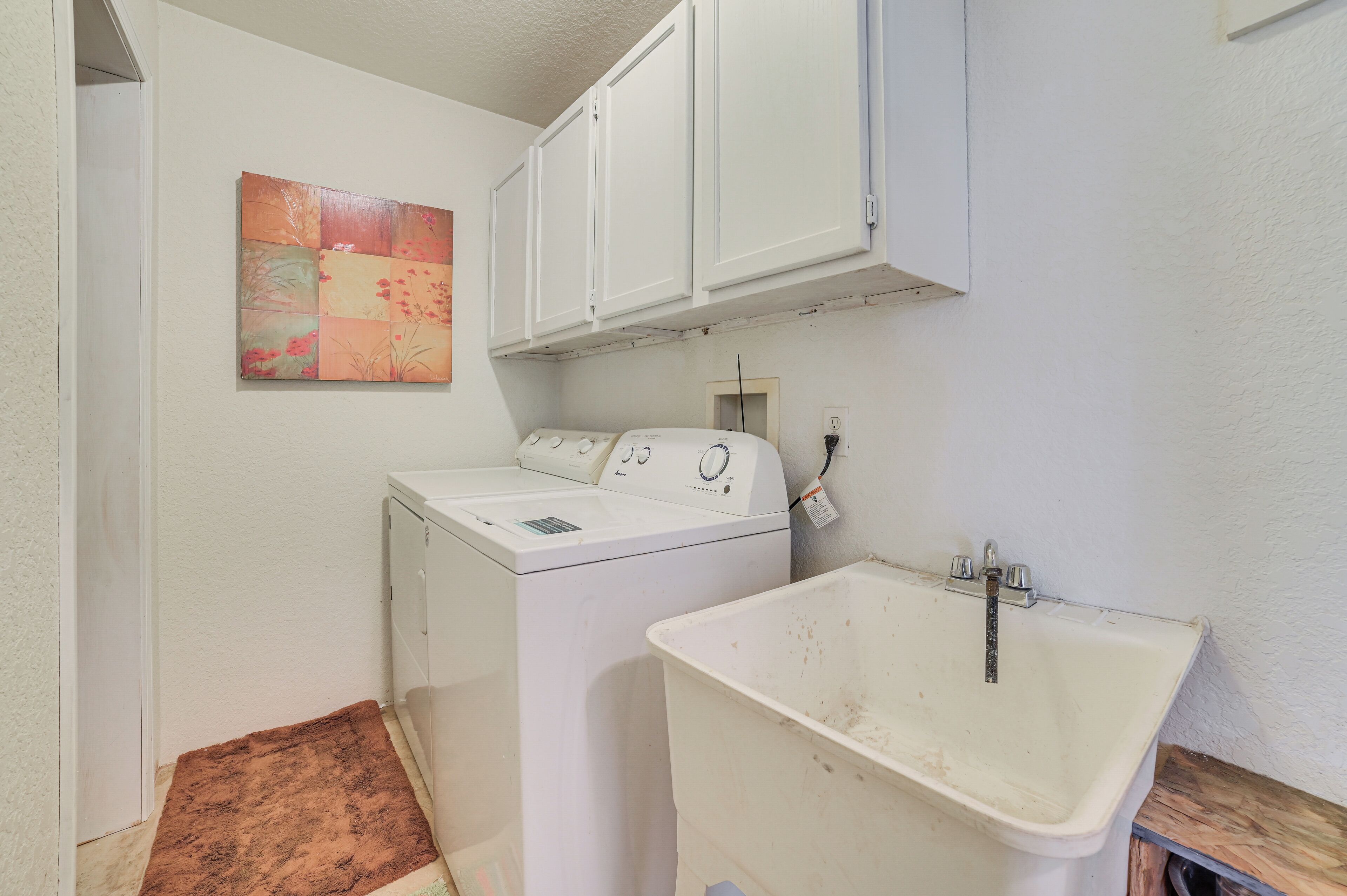 A laundry area with a washing machine, a sink, and a cabinet above the machine.