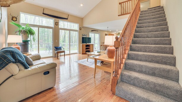 Un salón amplio con escalera de madera, un sofá, una mesa de centro y un ventanal que ofrece vistas al exterior.