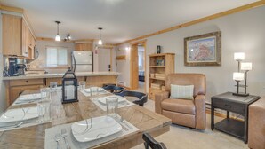 A modern kitchen with wooden cabinets, a dining area with a wooden table set for four, and a cozy seating area with a leather chair and a small side table.