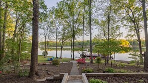 Un sentier en bois mène à une jetée au bord d’un lac paisible, entouré d’arbres et d’un petit jardin.