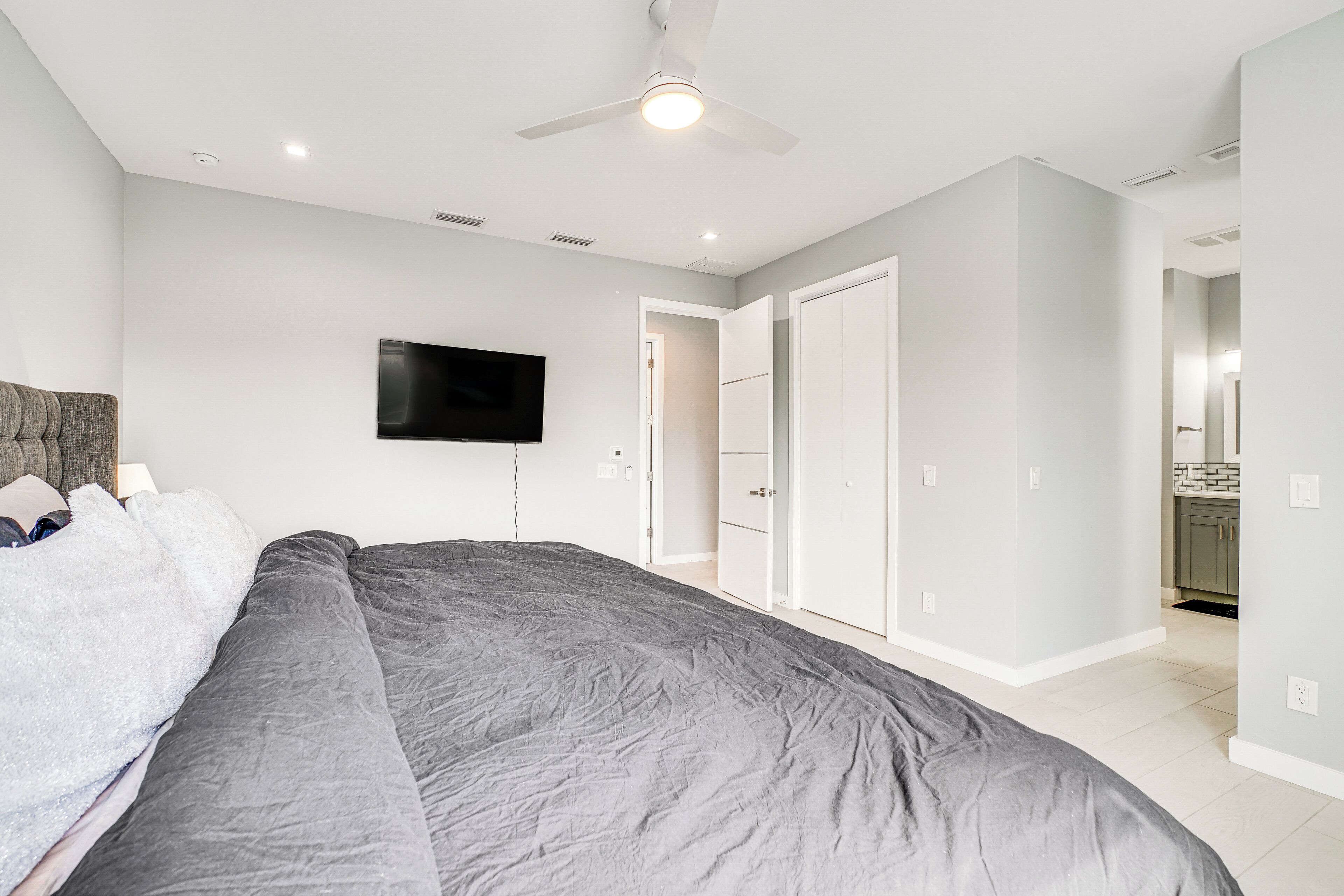 Un dormitorio con una cama grande, un ventilador de techo, un televisor de pantalla plana y un vestidor.