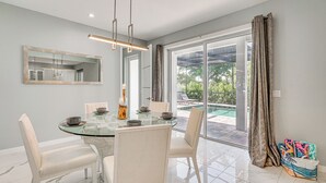 Un espace repas moderne avec une table en verre, des chaises blanches et un grand miroir au mur.