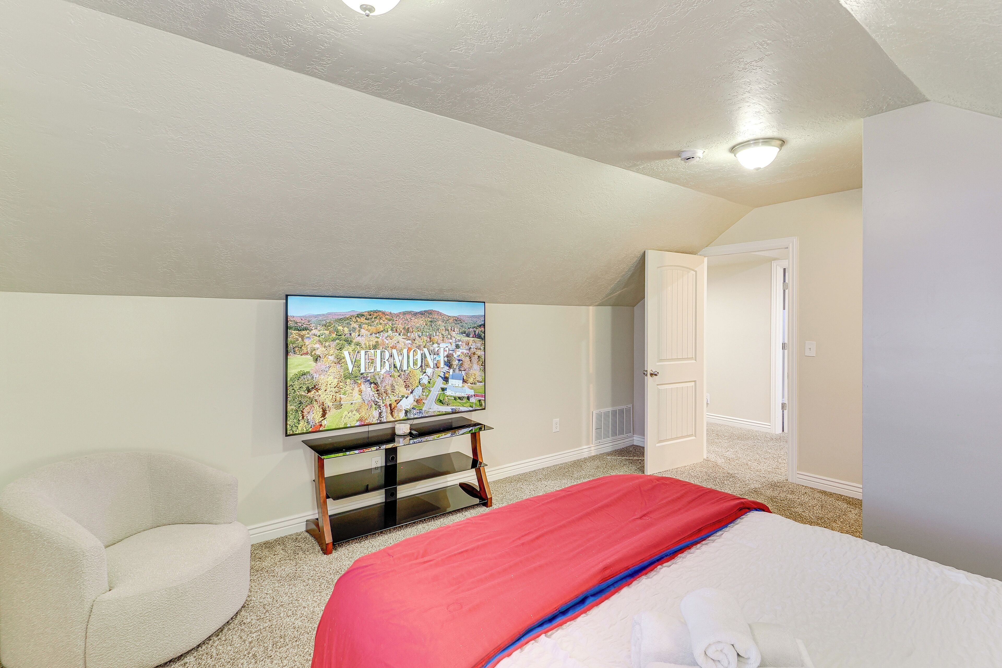 A bedroom with a bed, a TV mounted on the wall, a chair, and a door.