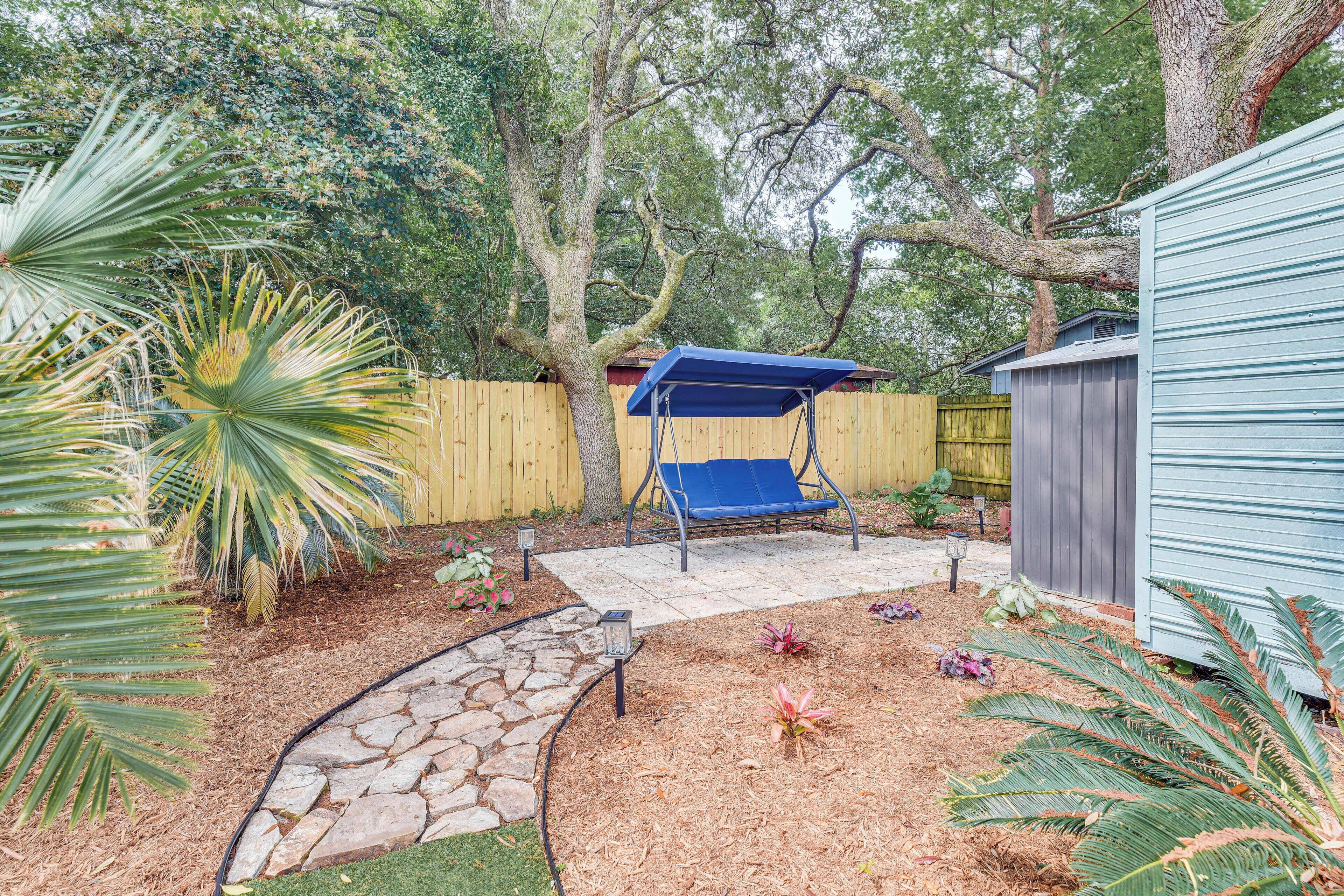 A backyard with a swing set, a stone pathway, and a wooden fence.
