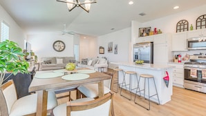 A modern kitchen with a central island, bar stools, and a dining area with a table and chairs. - Furnished Lanai & Golf Cart: the Villages Home! (Wildwood)