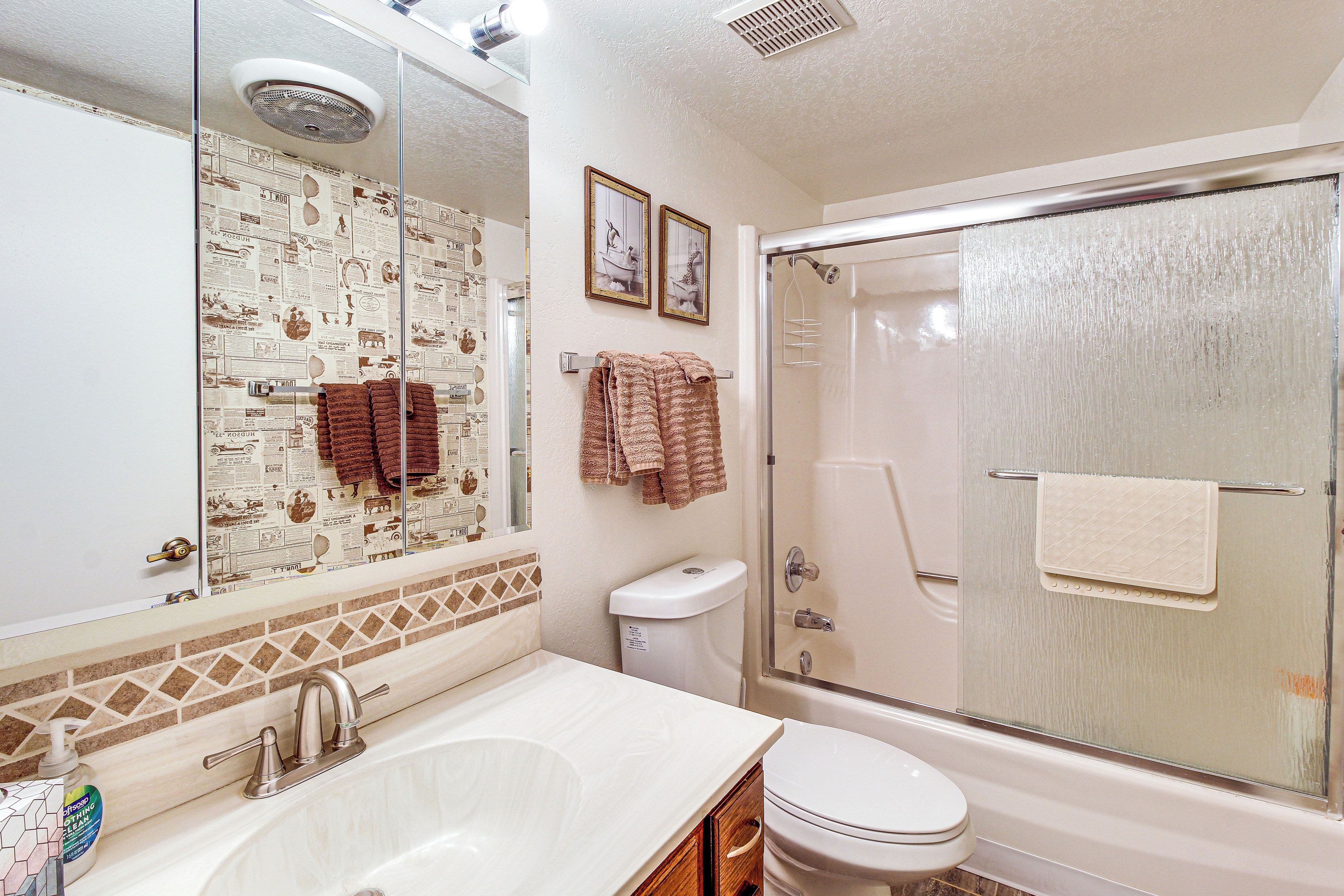 A bathroom with a glass-enclosed shower, a white sink, a toilet, and a mirror with a newspaper-themed backsplash.