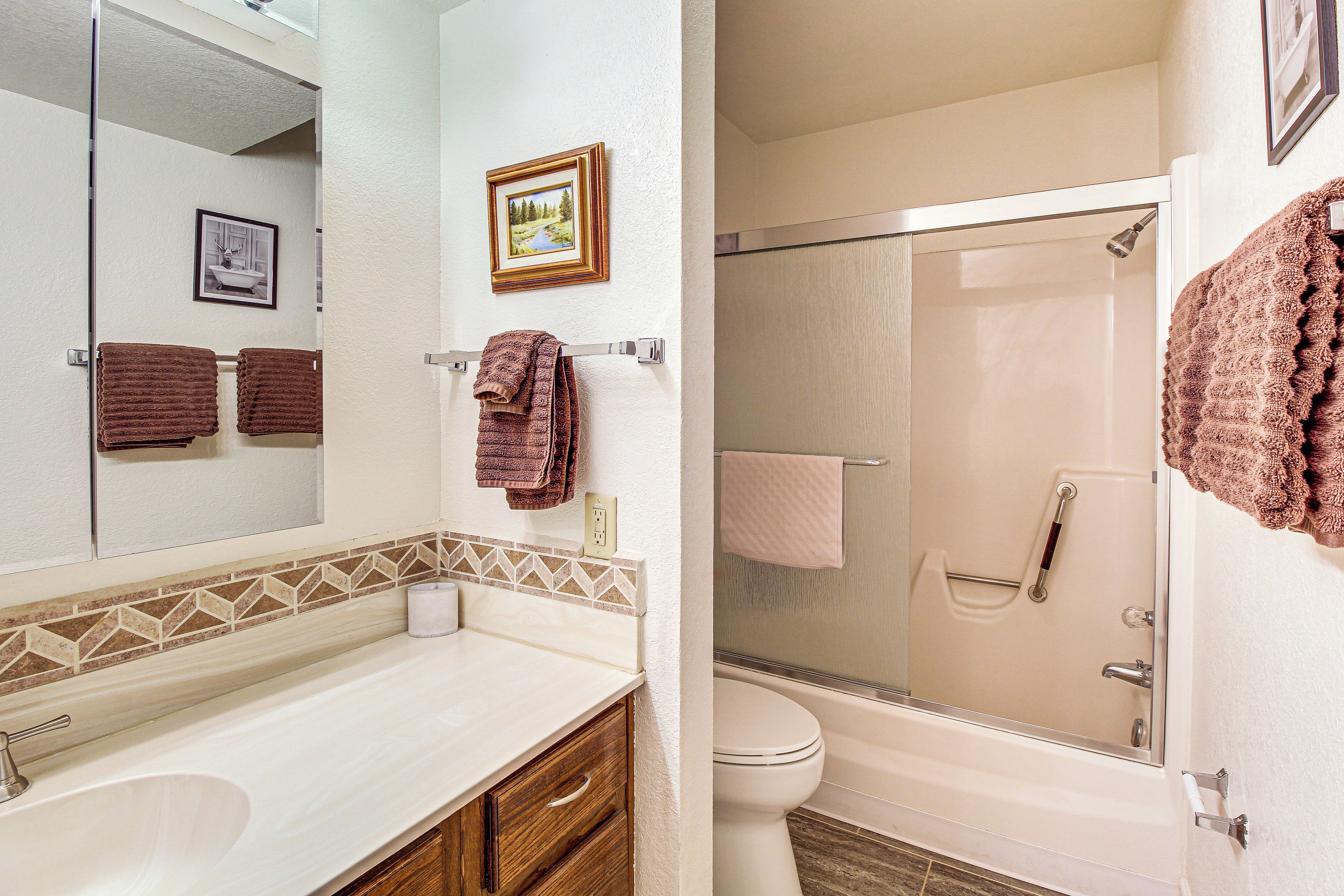 A bathroom with a sink, mirror, and toilet. There are towels hanging on the wall and a shower area.