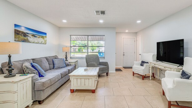 A living room with a grey sofa, a white coffee table, a TV, and a window with a view of greenery. - 5 Mi to Weeki Wachee! Home w/ Lanai & Air Hockey (Spring Hill)