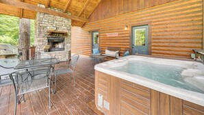 Una cabaña de madera con chimenea de piedra, jacuzzi y mobiliario para exteriores.