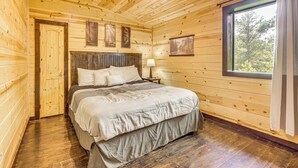 Dormitorio de cabaña de madera con cama, mesita de noche y ventana con cortinas.