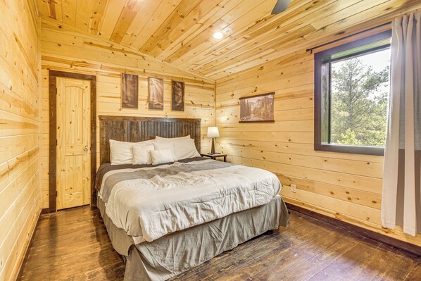 A wooden cabin bedroom with a bed, a nightstand, and a window with curtains.