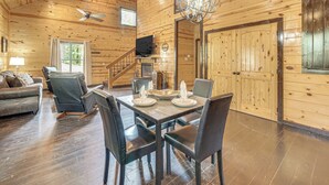 Interior de una cabaña de madera con comedor, sofá, televisión y escalera.