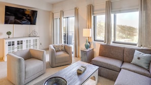 A living room with a sofa, armchairs, a coffee table, a TV, a cabinet, and a window with curtains.