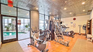 A gym with various exercise equipment, a pool visible through the glass doors, and a ceiling with a unique design.